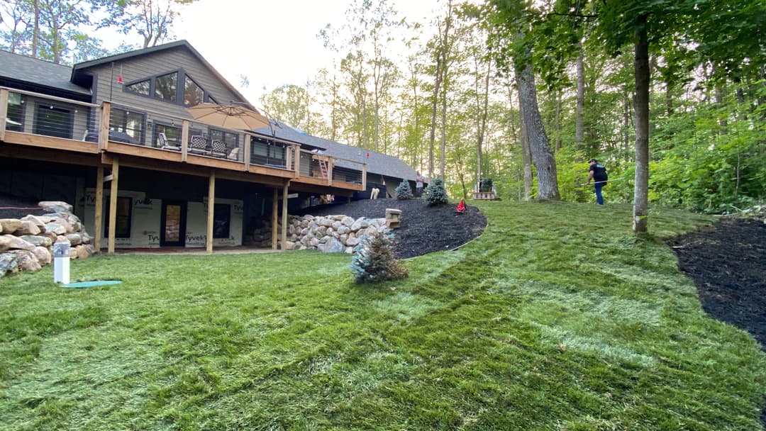 Lush green lawn with landscaped backyard and wooden deck near a forested area.