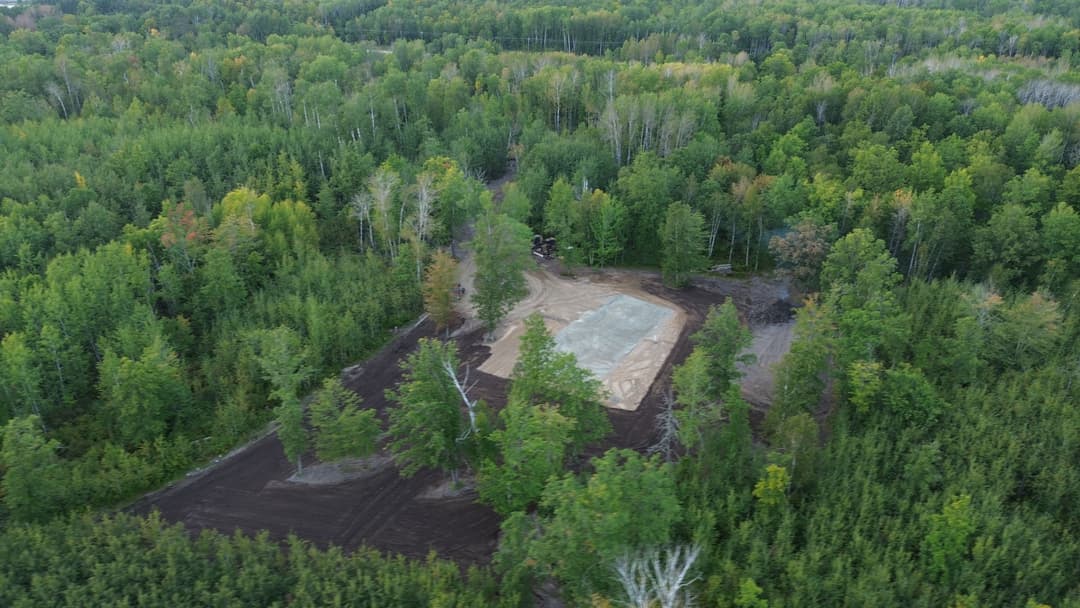 Aerial view of a cleared area in a lush green forest with trees surrounding the site.