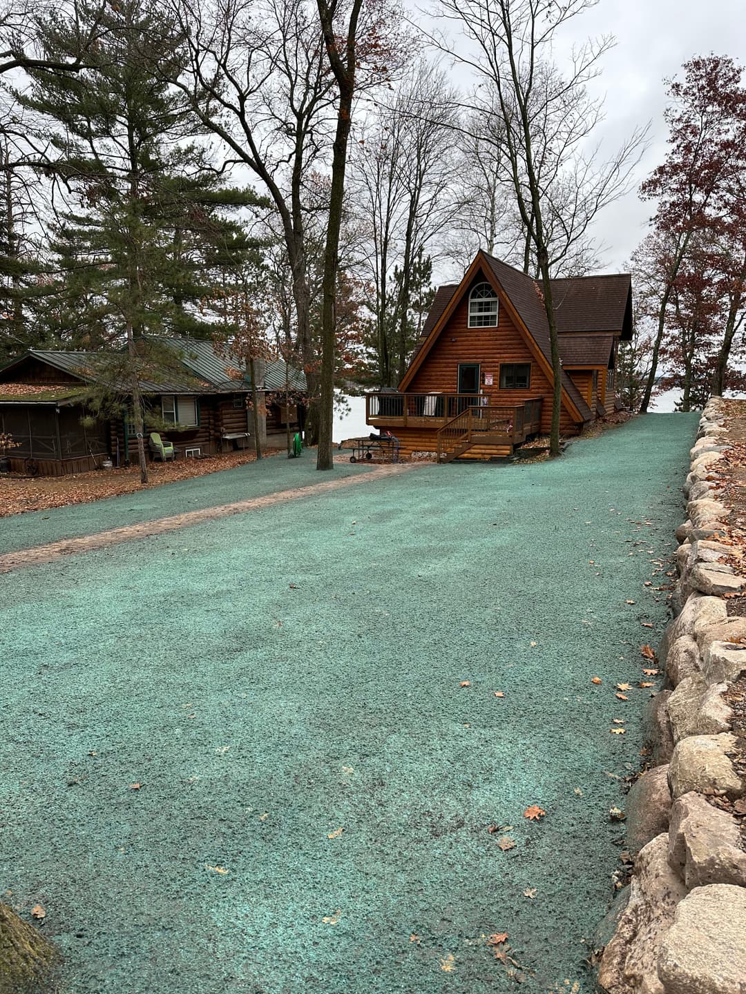 Cozy log cabin surrounded by trees on a gravel driveway near a lake in autumn.