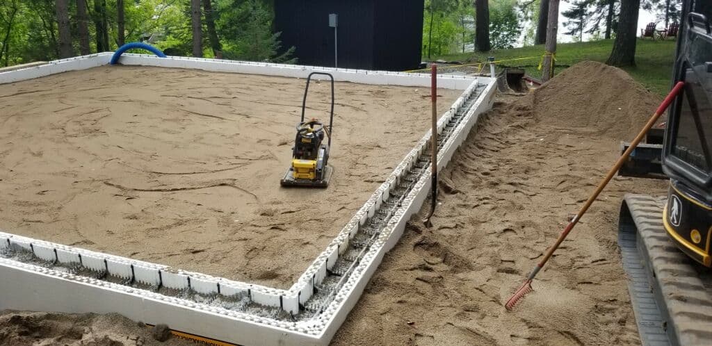 Construction site with a compacting machine on a prepared sand foundation for a new structure.