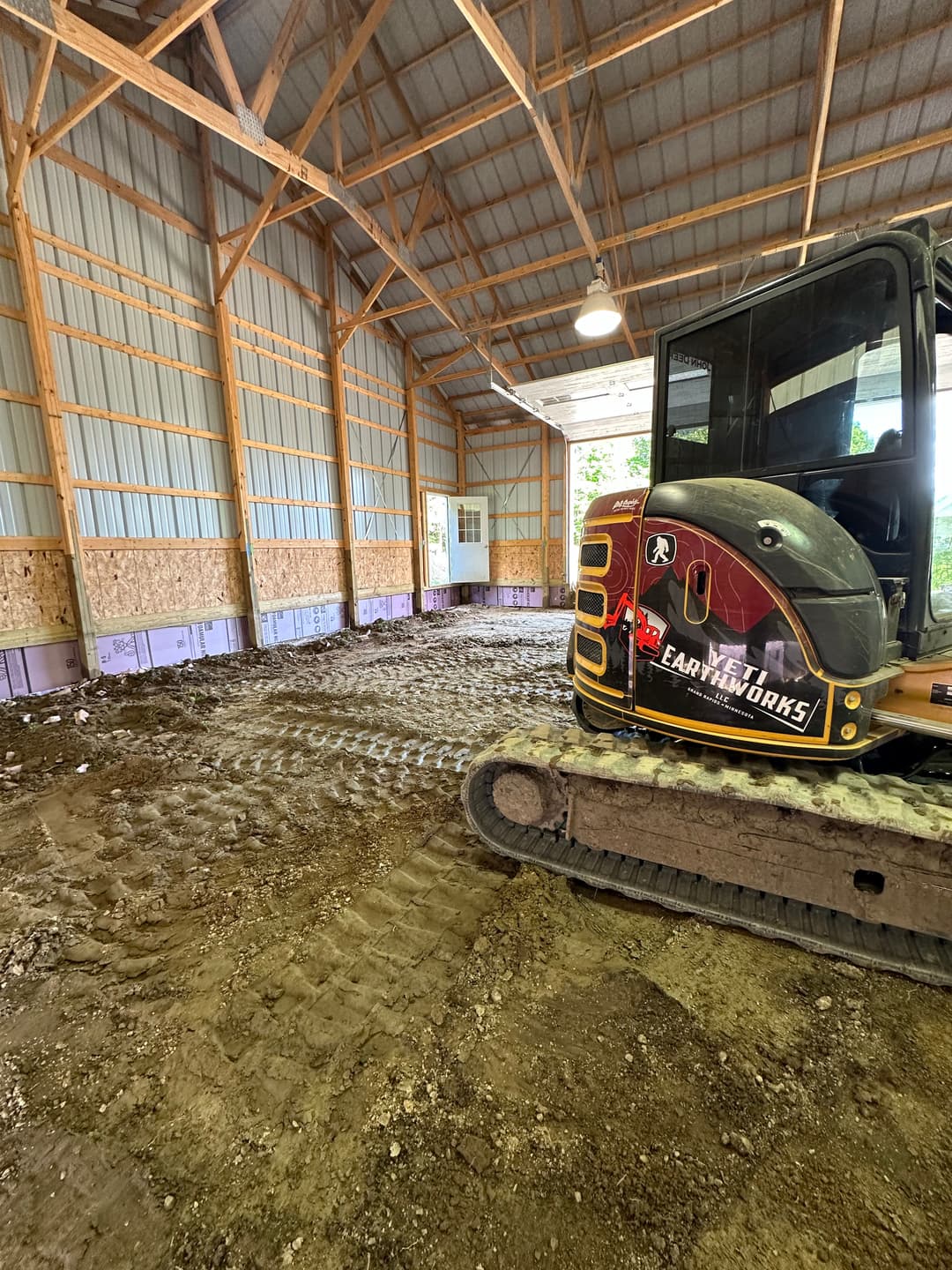 Excavator inside a spacious barn with dirt floor and wooden beams. Preparing for construction.