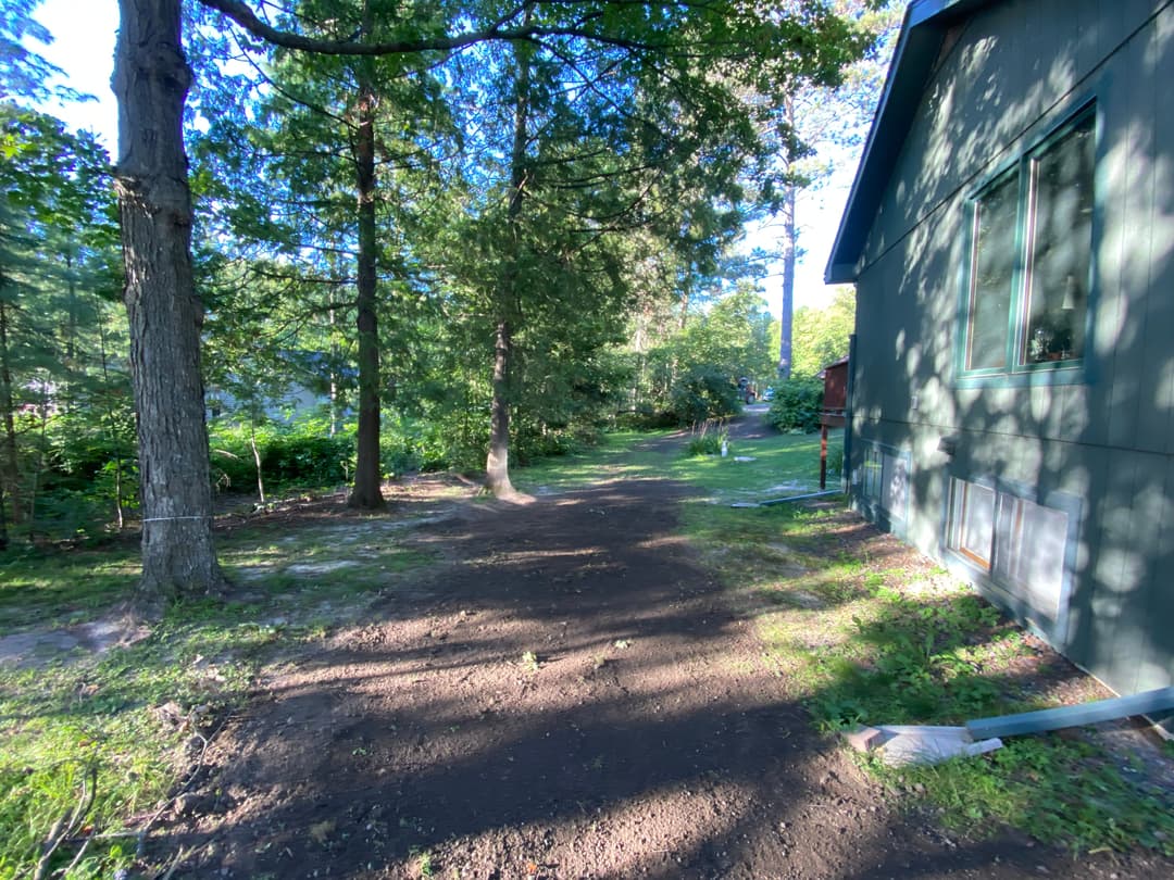 Pathway through trees leading to a green house, surrounded by natural surroundings.