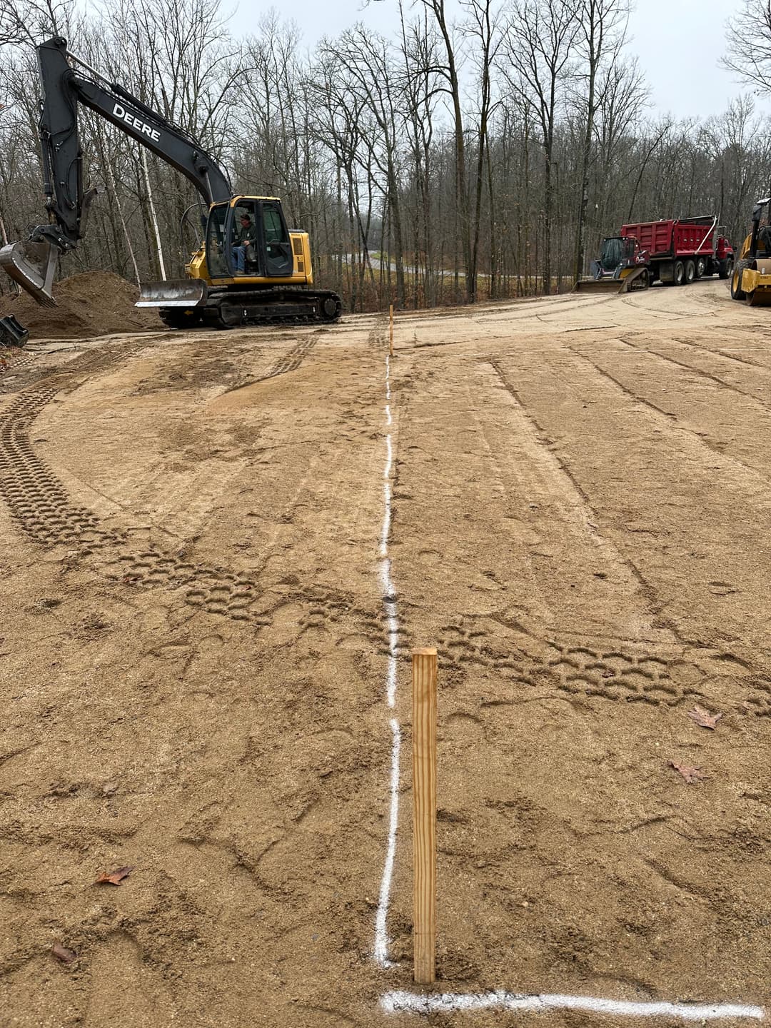 Excavator and construction equipment at a prepared gravel site with marked boundary lines.