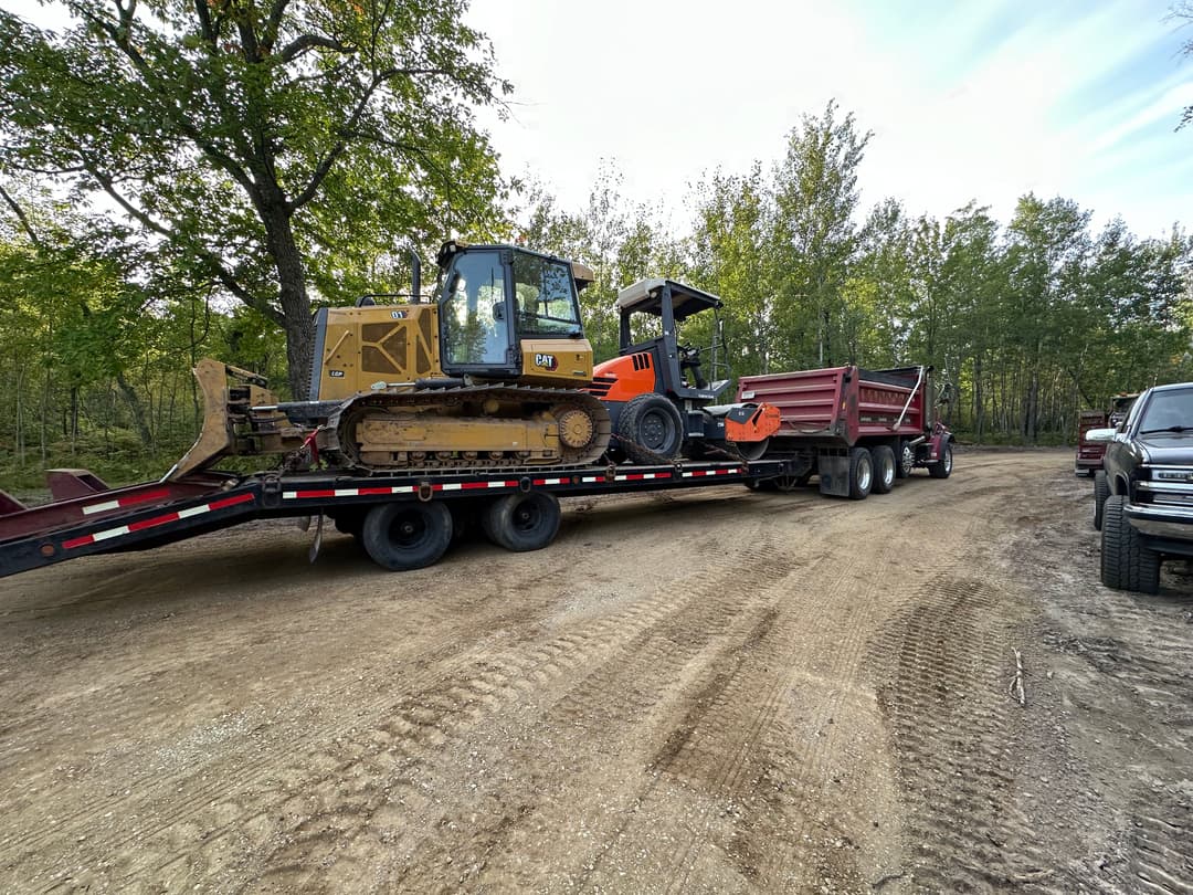 Bulldozer and tractor loaded on flatbed trailer in forested area, ready for transport.